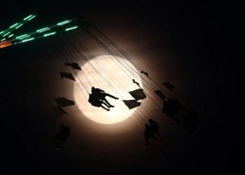 People on a funfair ride are silhouetted against the moon a day before the supermoon spectacle, in London